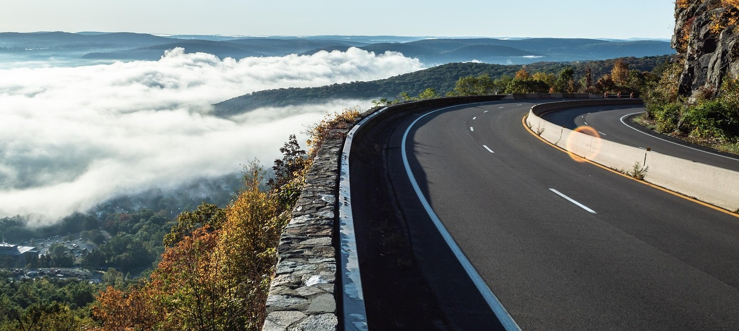 Scenic mountain road curving along a cliff above a fog-filled valley at sunrise